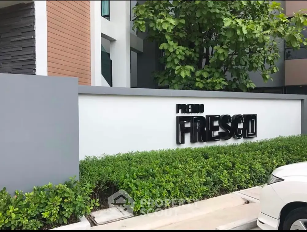 Modern residential building entrance with lush greenery and stylish signage.