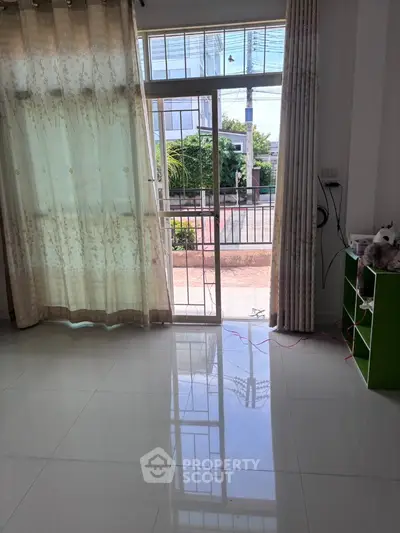 Bright living room with large windows and tiled floor, offering a view of the garden.