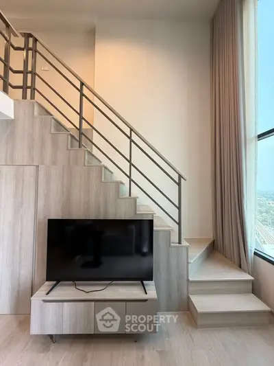 Modern living room with stylish staircase and large window offering natural light.