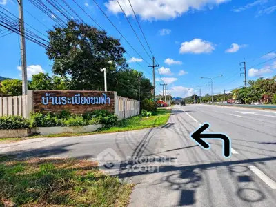 Scenic road view with real estate sign and lush greenery under a clear blue sky.
