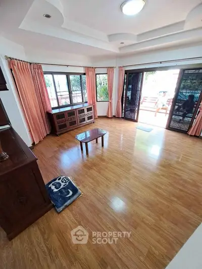 Spacious living room with wooden flooring and large windows opening to a balcony.