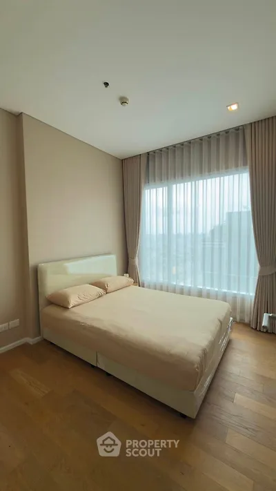 Spacious bedroom with large window and elegant curtains in modern apartment.