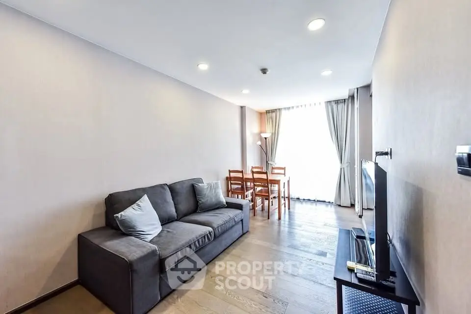 Modern living room with cozy sofa and dining area, featuring elegant wooden flooring and natural light.
