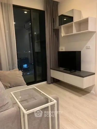 Modern living room with sleek furniture and large window offering city views.