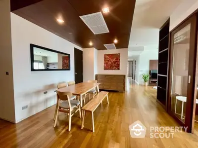 Spacious dining area with polished hardwood floors, modern lighting, and a sleek wooden dining set, leading to a bright, open living space.