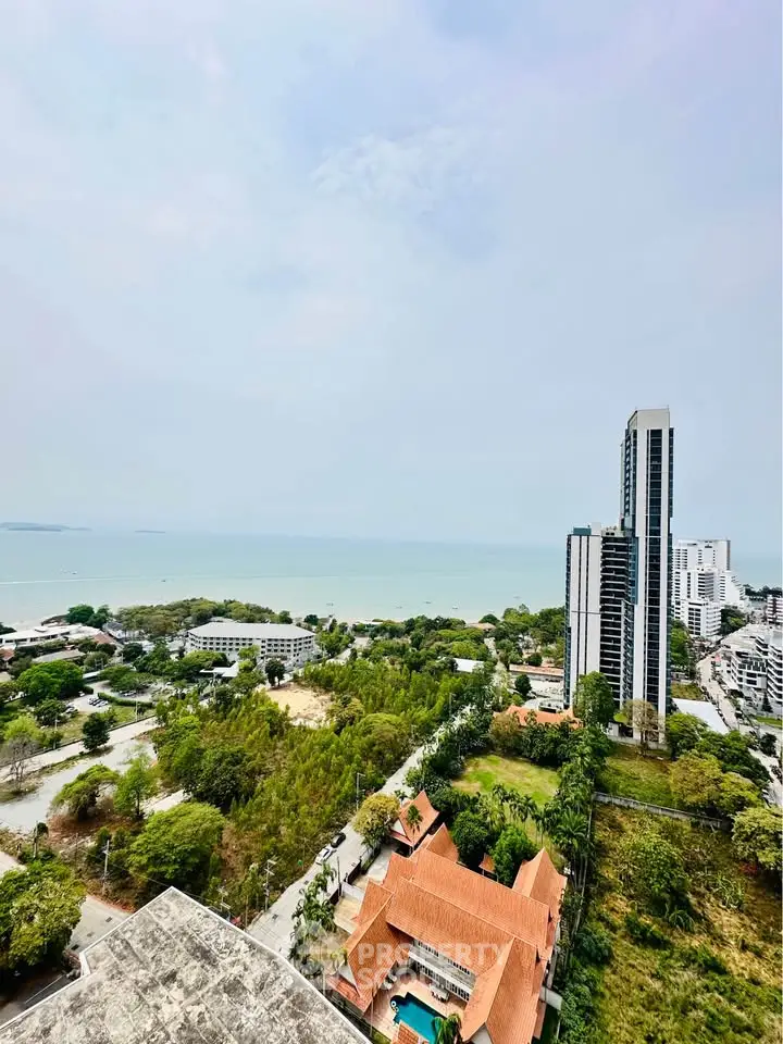 Stunning high-rise view of coastal cityscape with ocean horizon, lush greenery, and modern buildings.
