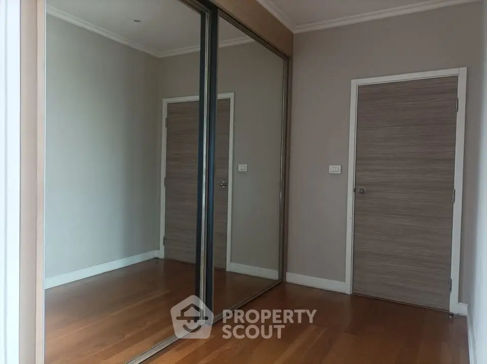 Spacious room with mirrored closet doors and wooden flooring