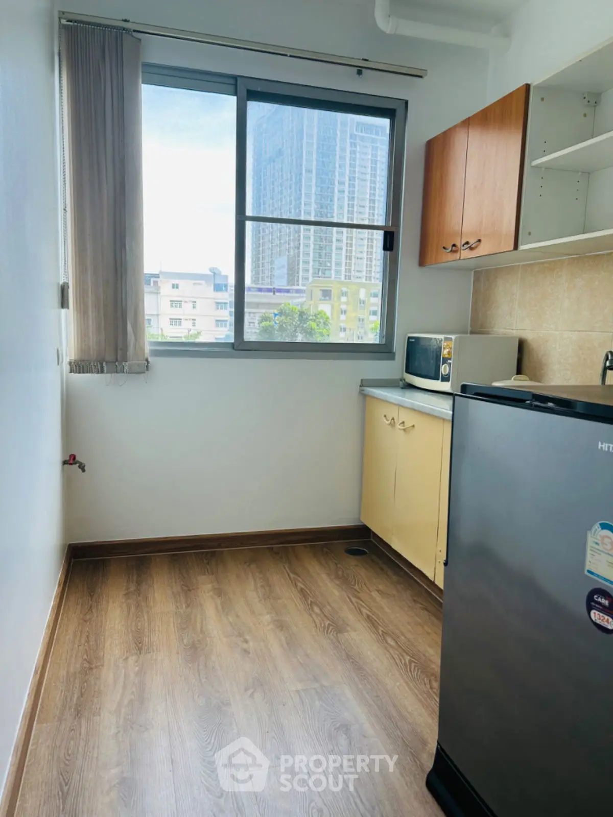 Compact kitchen with wooden flooring and city view, featuring a fridge and microwave.