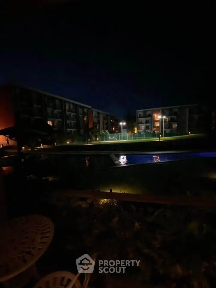 Night view of residential complex with illuminated pool and surrounding buildings.
