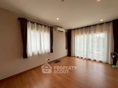 Spacious living room with large windows and wooden flooring, perfect for natural light and comfort.