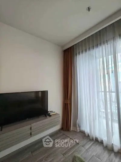 Modern living room with TV and large window, featuring elegant curtains and sleek flooring.