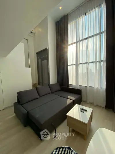 Modern living room with high ceilings and large windows offering natural light and city views.