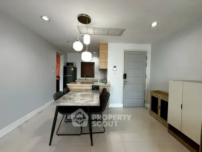 Modern dining area with sleek table, stylish lighting, and open kitchen layout in a contemporary apartment.