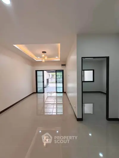 Spacious modern living room with glossy tiled floors and elegant lighting, leading to a bright outdoor view.