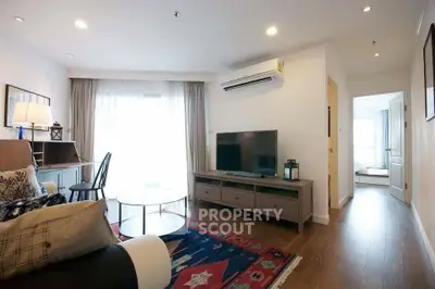Modern living room with stylish decor, large TV, and natural light from window.