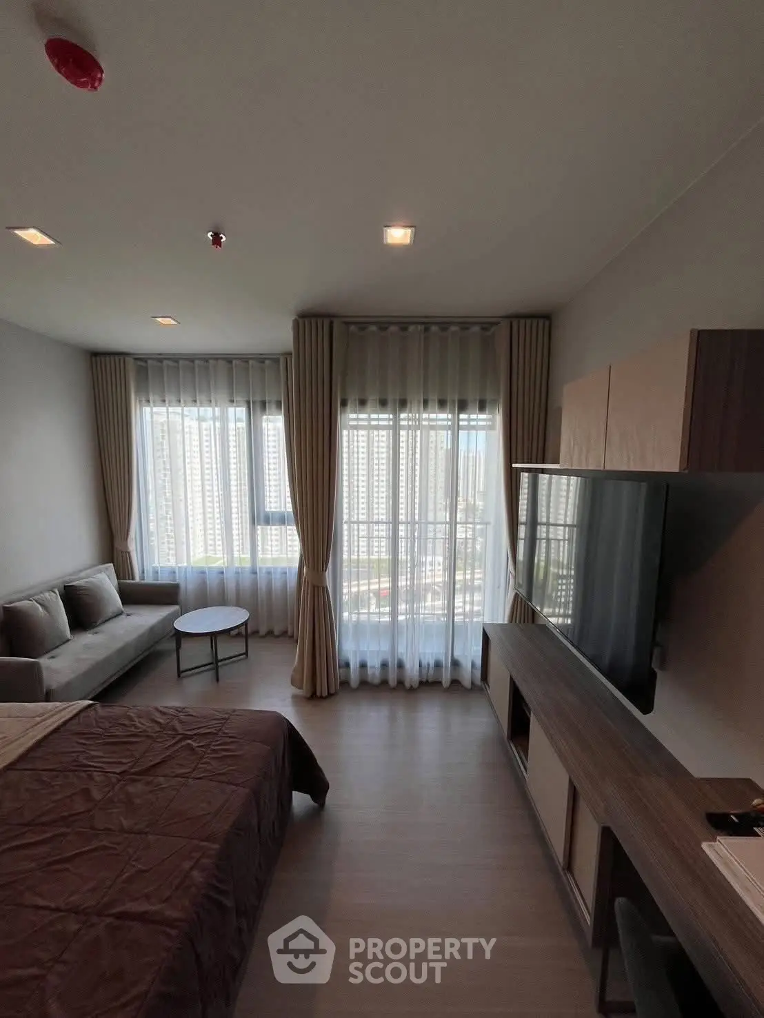 Modern studio apartment with large windows and city view, featuring a cozy living area and sleek furnishings.