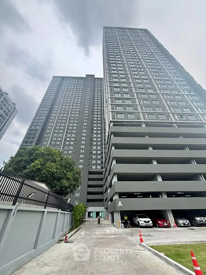 Modern high-rise residential building with spacious parking area and urban skyline view.
