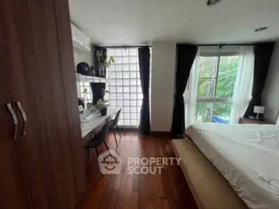 Chic bedroom with wooden flooring, modern desk, and lush garden view through large windows.