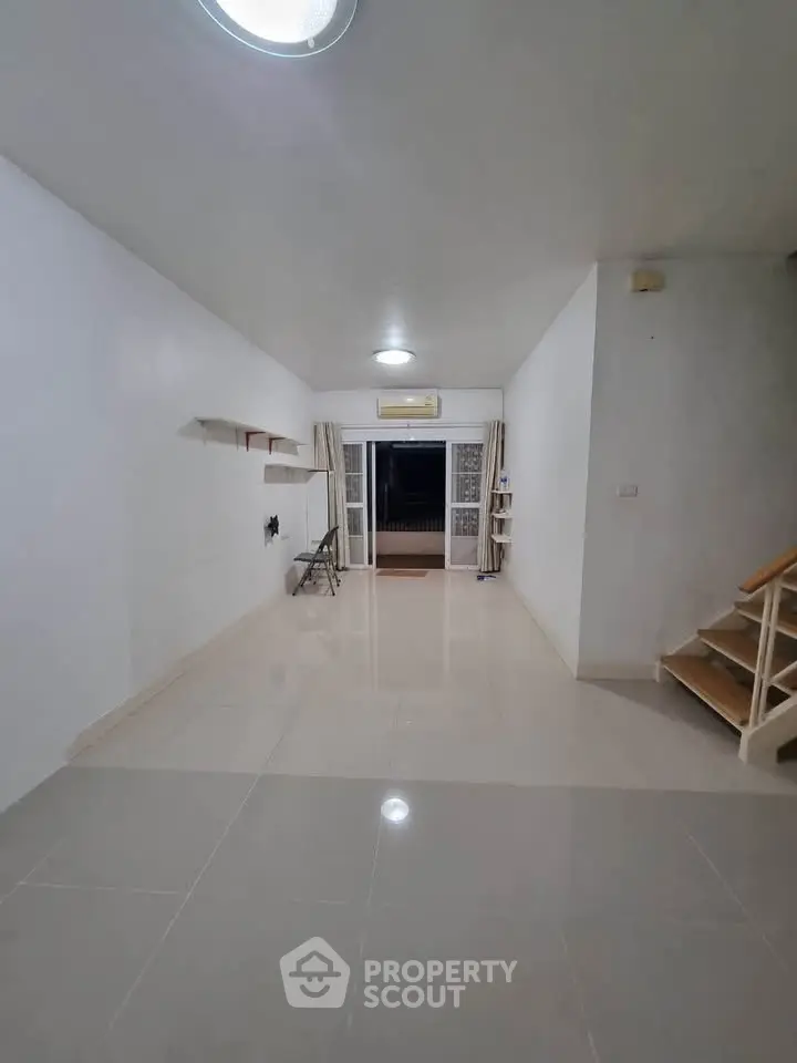 Spacious empty room with tiled flooring and staircase, ideal for customization.