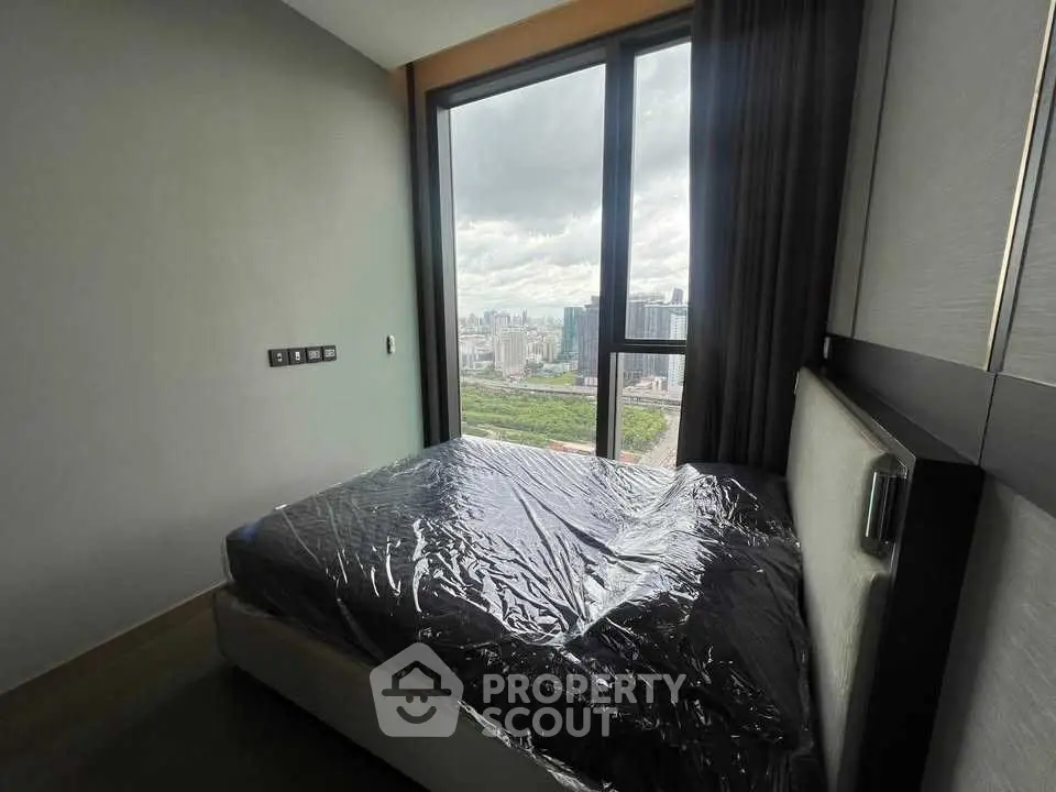 Modern bedroom with large window offering stunning city view, featuring a sleek bed with protective cover.