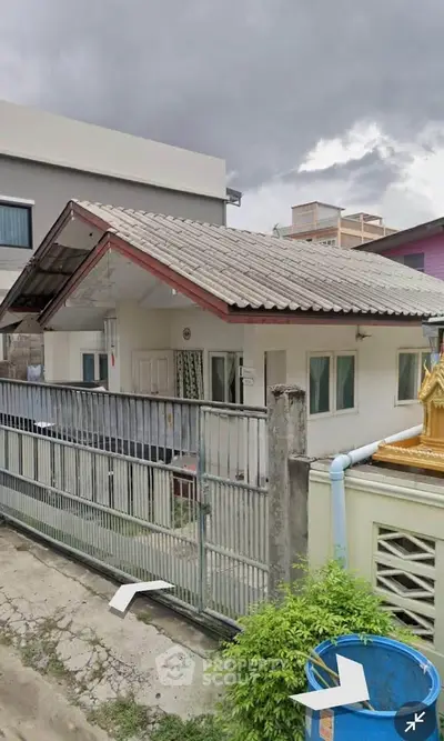 Charming single-story home with gated entrance and sloped roof under cloudy skies.