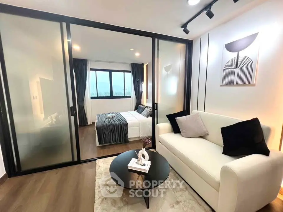 Modern living room with glass partition leading to a stylish bedroom, featuring elegant decor and cozy ambiance.