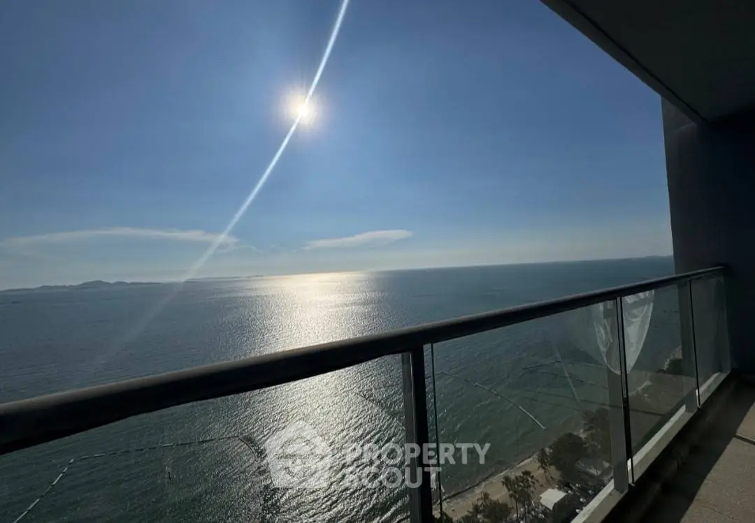 Stunning ocean view from a high-rise balcony with glass railing and clear blue sky.