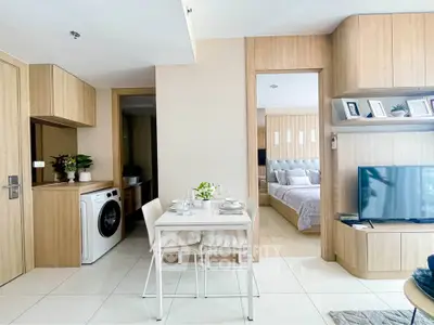 Modern open-plan living room with dining area and washing machine, featuring sleek wooden cabinetry and cozy bedroom view.