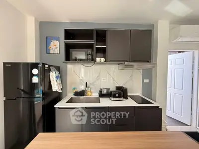 Modern kitchen with sleek black cabinets and appliances, featuring a double sink and stylish decor.