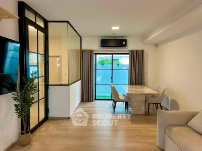 Modern living room with glass partition, stylish dining area, and large windows for natural light.