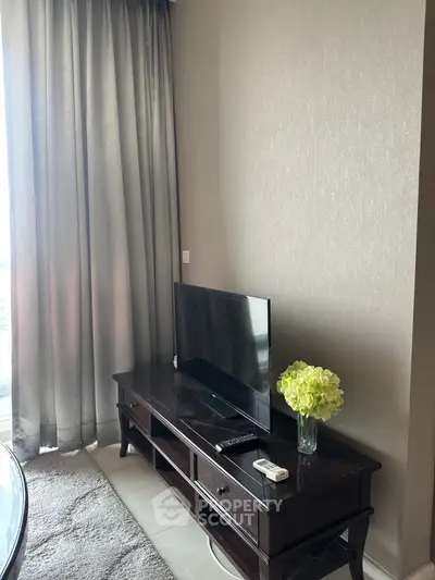 Cozy living room corner with TV stand, elegant curtains, and fresh flowers.