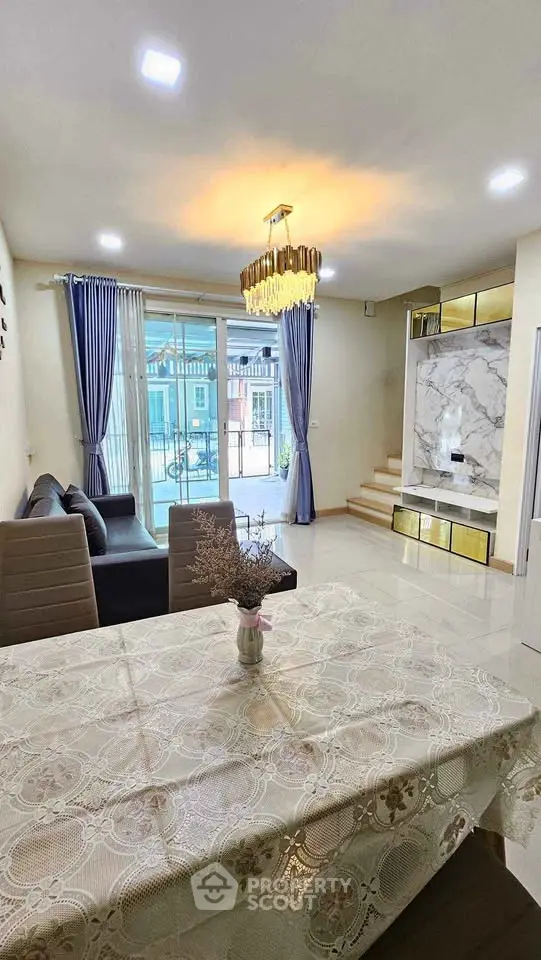 Elegant living room with modern chandelier and large windows, featuring stylish furniture and a cozy atmosphere.