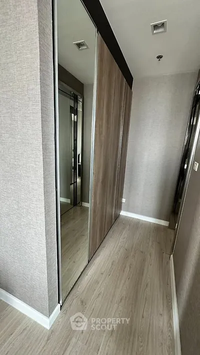 Modern hallway with mirrored closet doors and wood flooring in a stylish apartment.