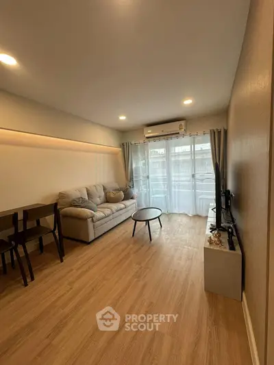 Modern living room with cozy sofa, wooden flooring, and natural light from large windows.