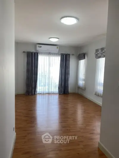 Spacious empty room with wooden flooring and large windows for natural light