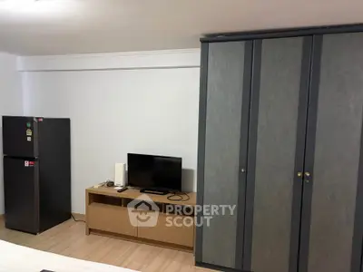Modern bedroom with sleek wardrobe, compact TV setup, and a mini fridge for convenience.