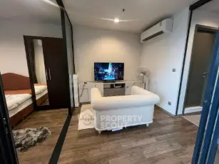 Modern living room with cozy white sofa and TV, adjacent to a bedroom with wooden flooring.