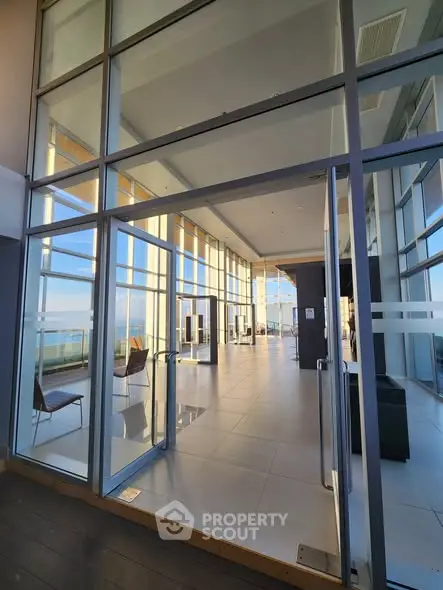Stunning modern building entrance with floor-to-ceiling windows and ocean view.
