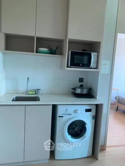 Compact kitchen with washing machine and microwave in modern apartment