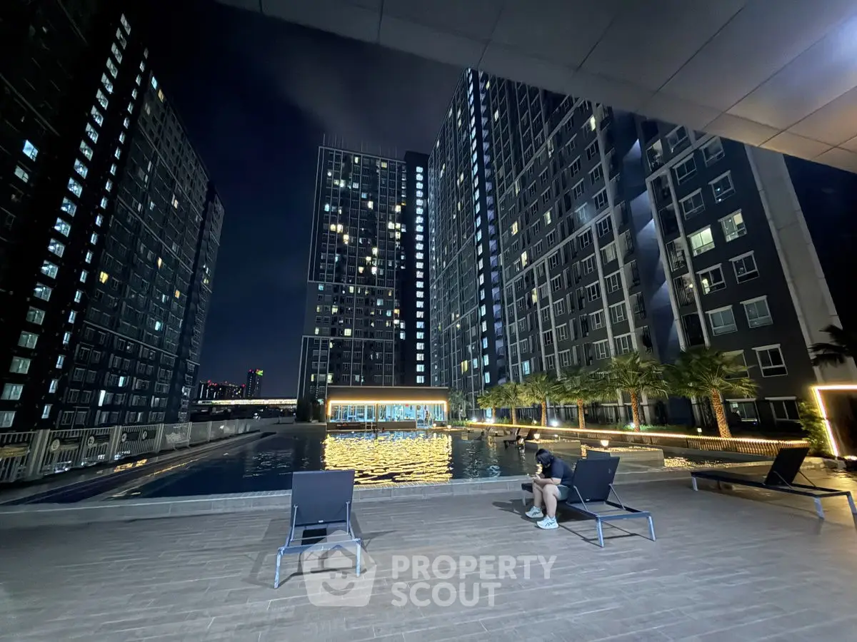 Stunning night view of modern high-rise apartment complex with illuminated pool and lounge area.