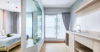 Modern apartment interior with bedroom and kitchenette, featuring large windows and natural light.