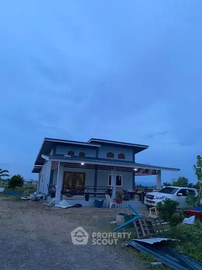 Modern two-story house with carport and outdoor seating area at dusk.