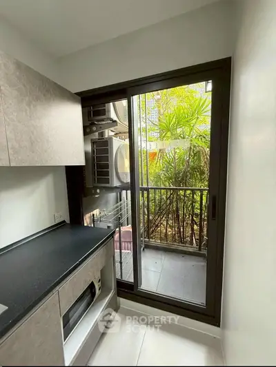 Modern kitchen with sleek cabinetry and sliding glass door leading to a lush balcony view.