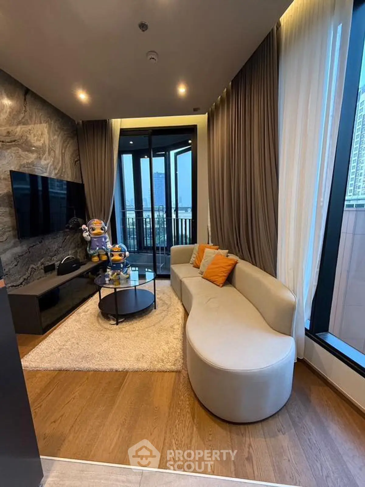Stylish modern living room with curved sofa and large TV, featuring floor-to-ceiling windows and city view.