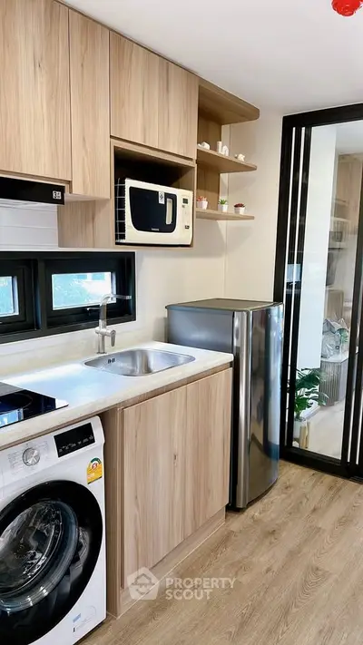 Modern kitchen with wooden cabinets, microwave, washing machine, and compact fridge in stylish apartment.