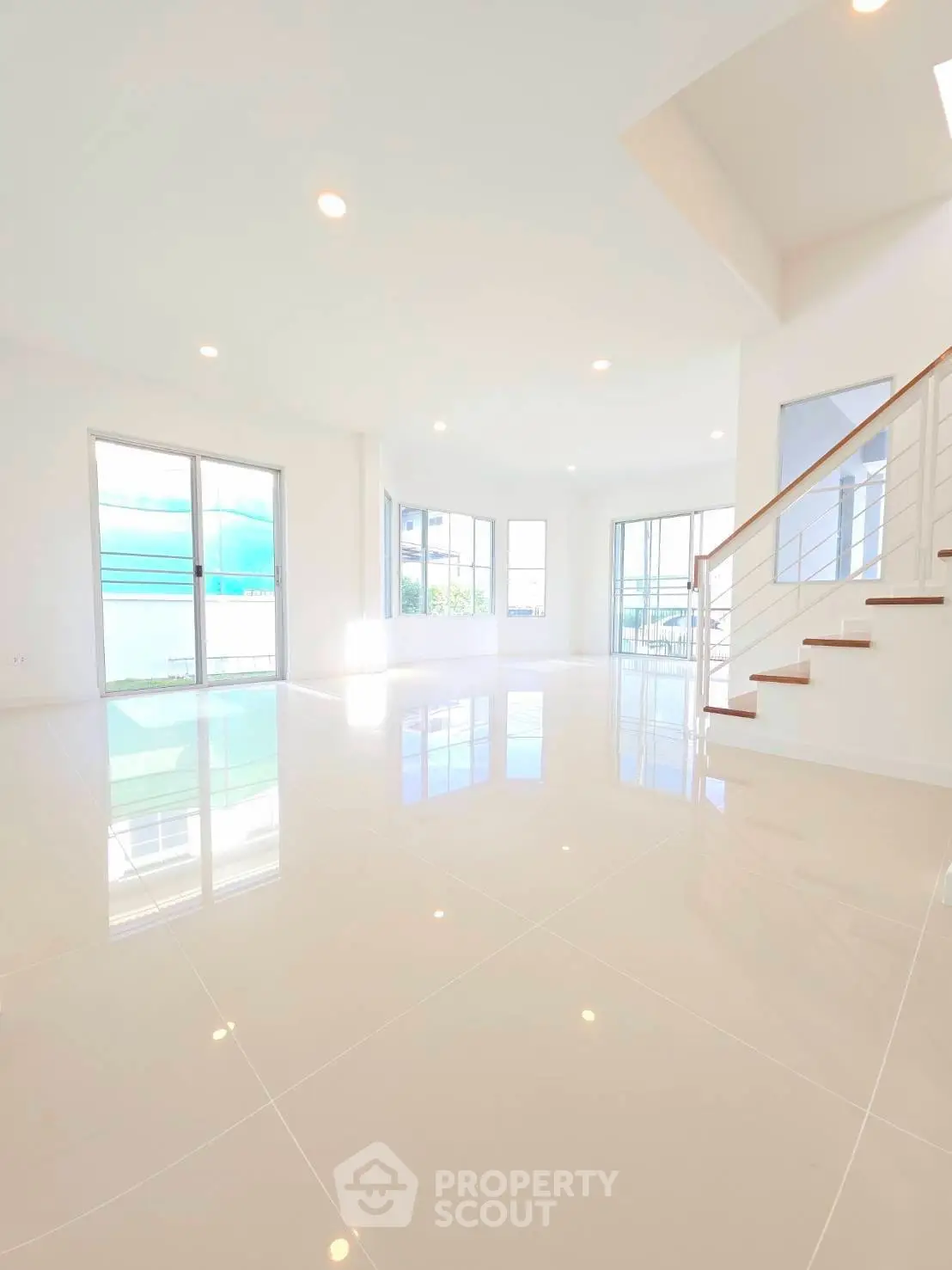 Spacious modern living room with large windows and elegant staircase, perfect for natural light lovers.
