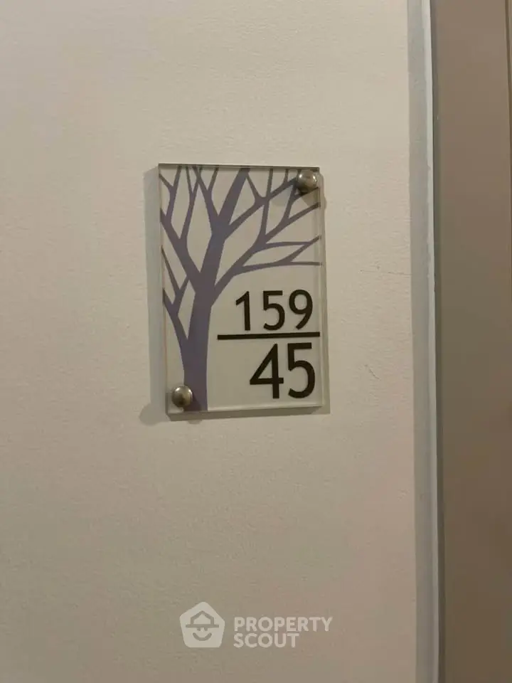 Modern apartment unit number sign with artistic tree design on wall.