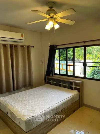 Cozy bedroom with ceiling fan and large window overlooking greenery.