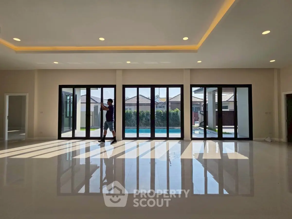 Spacious modern living room with floor-to-ceiling windows overlooking a pool, perfect for luxury living.