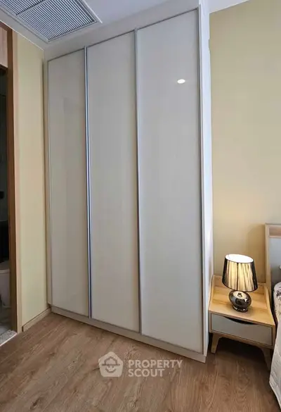 Modern bedroom with sleek wardrobe and stylish bedside lamp on wooden floor.